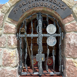 Schmiedeeisernes Denkmal der Heiligen mit Attributen auf dem Gitter. St. Birgitta von Schweden – Stab, St. Benedikt – Medaillon